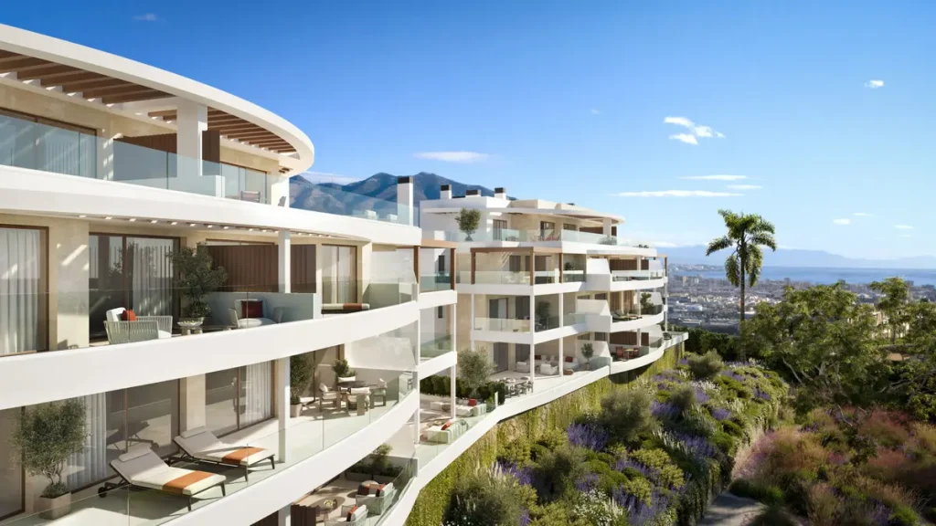 Modern white apartment building on a hillside with large curved balconies and panoramic views of the city, sea, and mountains.