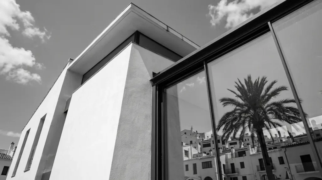 Black and white photo of a modern Spanish building facade next to a palm tree.